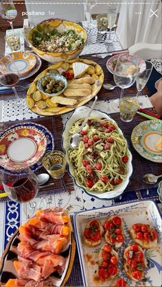 a table full of food including pasta, tomatoes and other foods on plates with utensils