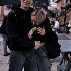 a man and woman standing next to each other on a sidewalk with an umbrella over their heads