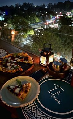 two slices of pizza sitting on top of a wooden table next to plates and cups