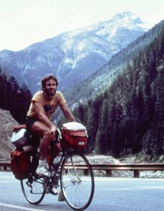 a man riding a bike down the middle of a road with mountains in the background