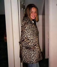 a woman standing in front of a door wearing a leopard print coat