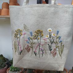 an embroidered bag with flowers and butterflies on it in front of some potted plants