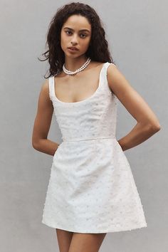 a woman in a short white dress with pearls on her neck and legs, posing for the camera