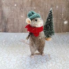 a toy mouse with a hat and scarf holding a small christmas tree in it's paws