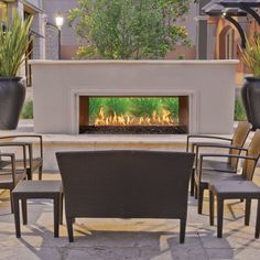 an outdoor fireplace with chairs around it and plants on the outside patio area in front of it