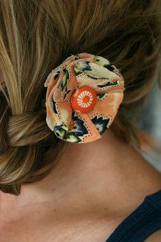 a close up of a woman with a flower in her hair, wearing an orange and black floral fabric brooch