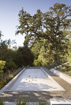 an empty pool in the middle of a garden with trees and bushes around it, surrounded by gravel