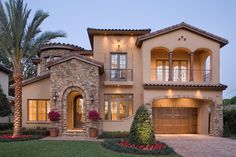 a large house with two garages and palm trees in the front yard at dusk