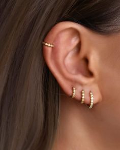 a woman wearing gold ear cuffs with small white stones on the end of each ear