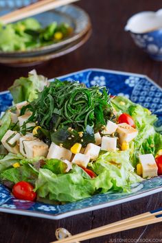 a salad with lettuce, tomatoes and tofu on a blue plate next to chopsticks