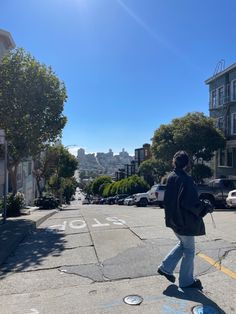 a man walking down the street in front of some parked cars and buildings on a sunny day