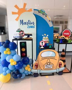 an orange vw bug parked in front of a blue and yellow balloon arch at a birthday party