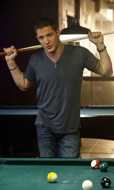 a man holding a pool stick while standing next to a pool table