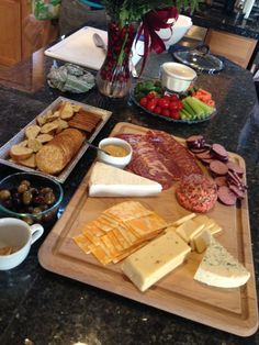 an assortment of cheeses, crackers and meats on a wooden cutting board