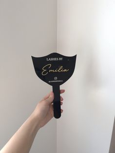 a person holding up a black fan with the words lashes by emila on it