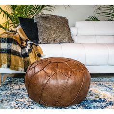 a living room with a white couch and brown leather pouffle on the floor