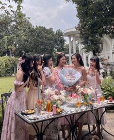 a group of women standing around a table with food and drinks on it in front of a white house