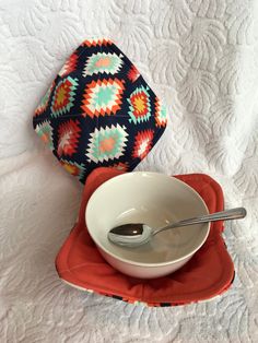 a bowl and spoon sitting on top of a red place mat next to a pillow