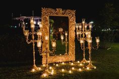 an elaborately decorated mirror and candles stand in the grass at night with lights on it