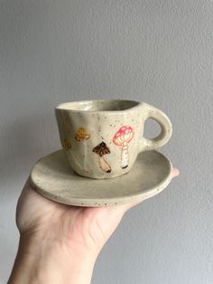 a hand holding a cup and saucer with mushrooms painted on the inside, in front of a white wall