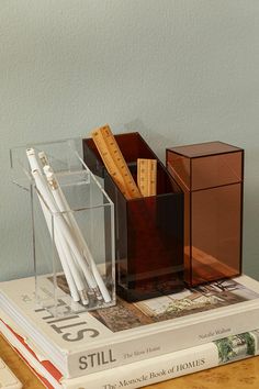 a stack of books sitting on top of a wooden table next to a pen and pencil holder