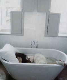 a woman laying in a bathtub next to a window