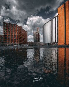 a body of water in front of tall buildings under a cloudy sky with dark clouds