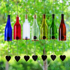 several different colored wine bottles hanging from strings in front of a window with trees behind them