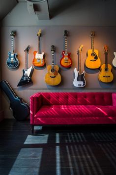 a room with guitars hanging on the wall and a couch in front of it,