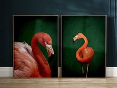 two flamingos standing next to each other in front of a green wall and wooden floor