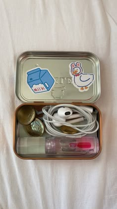 an open tin with various items in it on a white sheeted surface, including earbuds and plugs