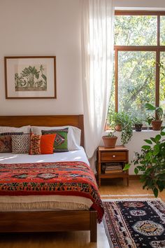 a bed sitting next to a window in a bedroom under a painting on the wall