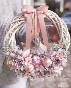 a person holding a wreath with pink flowers and a figure on it in the center