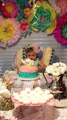 a baby sitting in a high chair next to a table with cakes and cupcakes