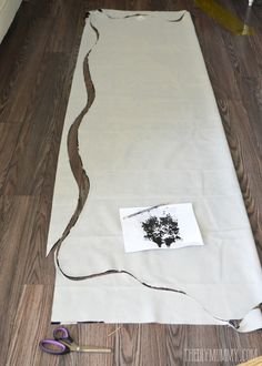 a piece of fabric is laying on the floor next to some scissors and yarn with a tree drawn on it