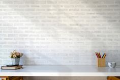 a white table topped with books and a vase filled with flowers next to a brick wall