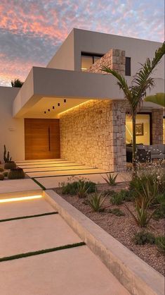 a modern house is lit up at night with lights on the side and palm trees in front