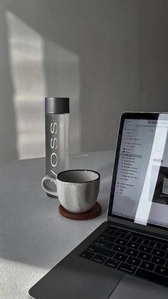 an open laptop computer sitting on top of a table next to a coffee cup and mug