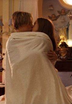 a man and woman kissing under a blanket in a room with angels on the walls