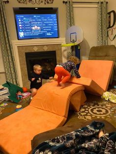 two children playing in a living room with couches and a tv on the wall