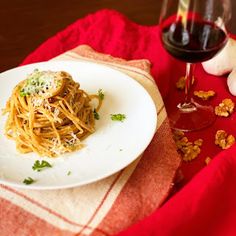 a white plate topped with pasta next to a glass of red wine and garlic florets