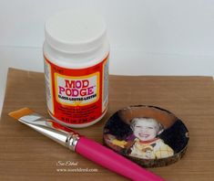 a pink paint brush next to a jar of food coloring and a small photo on a wooden surface