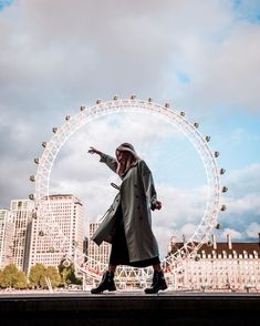 a woman is standing in front of a ferris wheel with her hand out to the side