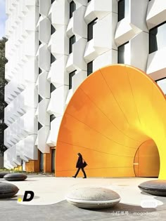 a person walking in front of a large yellow object on the ground next to a tall building