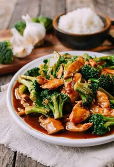 a white plate topped with chicken and broccoli covered in sauce next to rice