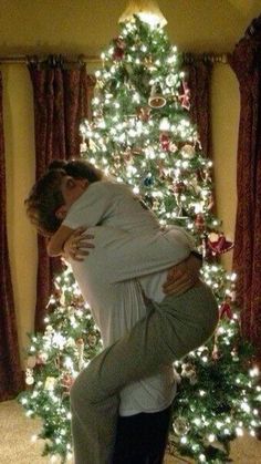 a man and woman are hugging in front of a christmas tree with lights on it