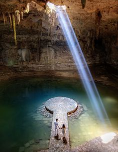 two people standing in front of a waterfall with a light beam coming from the top