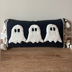 three white ghost pillows sitting on top of a wooden floor next to a black pillow