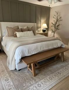 a bedroom with a large bed and wooden bench in the middle, along with two lamps on either side of the bed