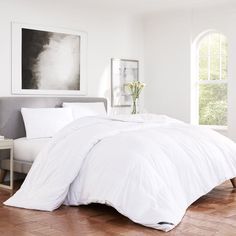 a bed with white sheets and pillows in a room next to a painting on the wall